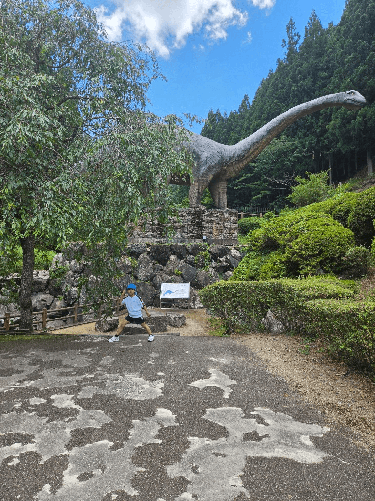 A student posing in front of a large sauropod dinosaur statue during an SSW Summer outing