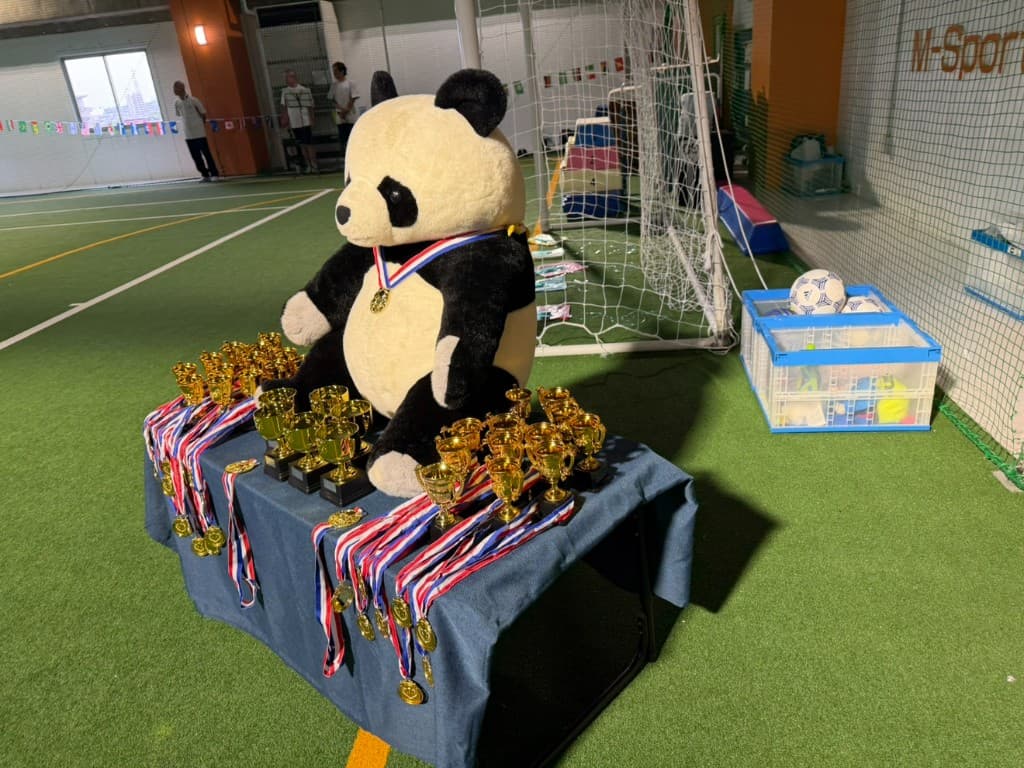 Sports Day trophies and medals displayed on a table with the TGA panda mascot at an indoor sports facility