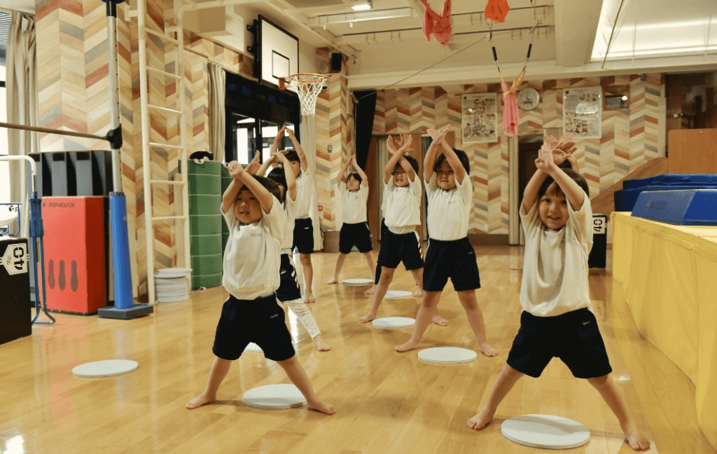 TGA students in PE uniforms raising their arms together during a coordinated gym activity