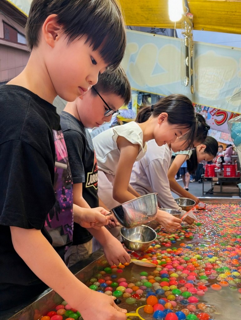 TGA students scooping colourful super balls from a water tank at a summer festival stall