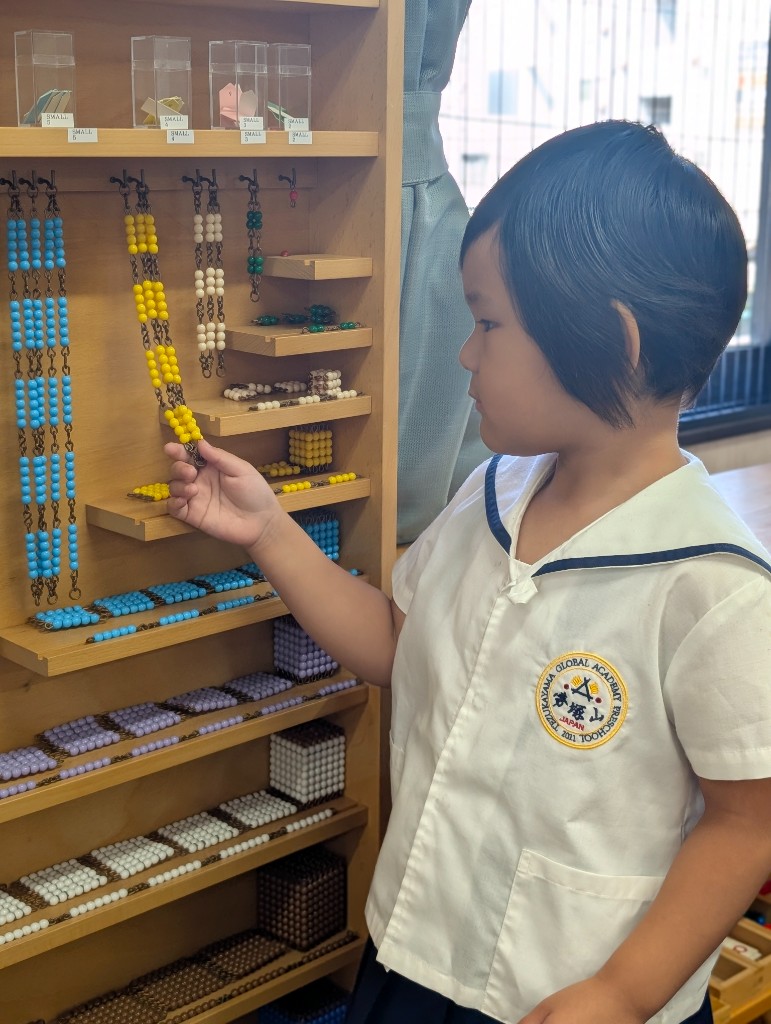 A student working with Montessori bead chains on a wooden shelf in the classroom