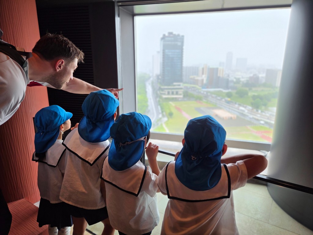 TGA students and teacher looking out over the Osaka city skyline from Abeno Harukas