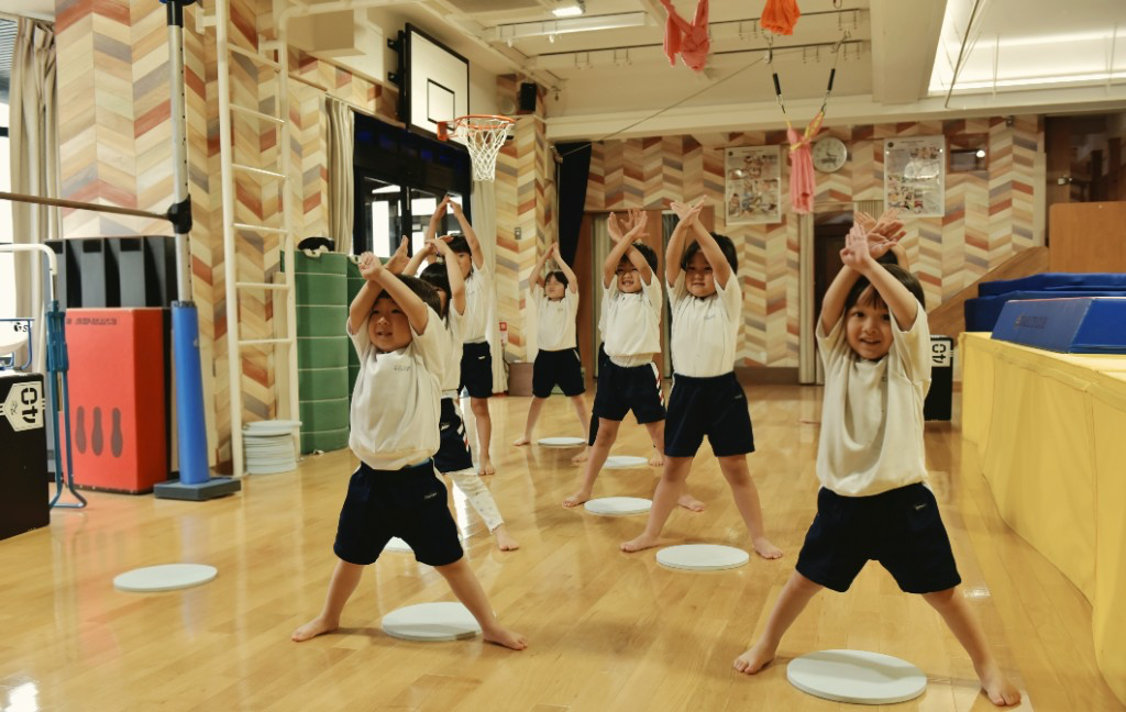 TGA students in PE uniforms raising their arms together during a coordinated gym activity