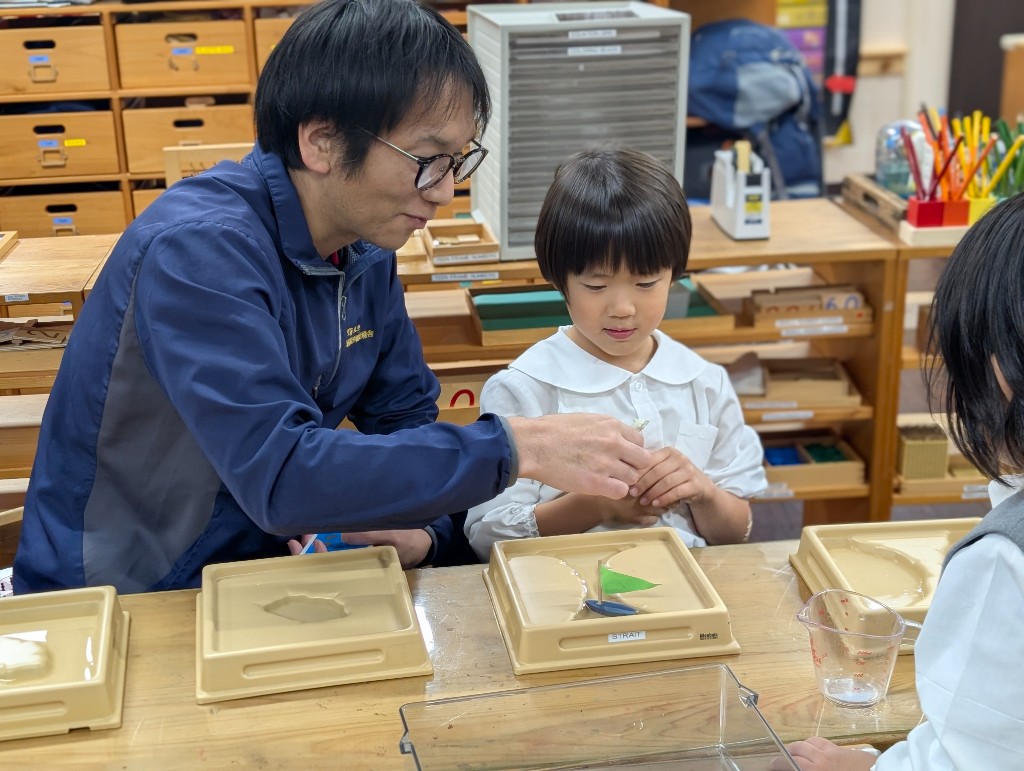 A teacher and student working together with Montessori land and water form trays in the classroom