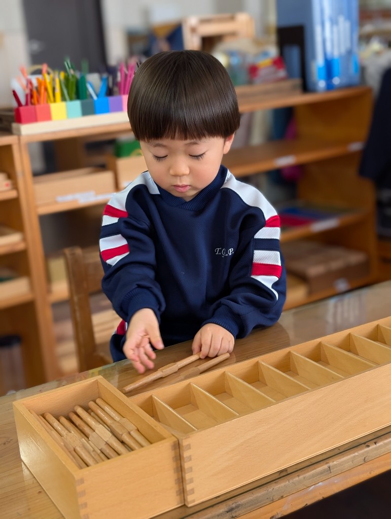 A young Tezukayama Global Academy student in a navy uniform focusing on a Montessori spindle rods math lesson